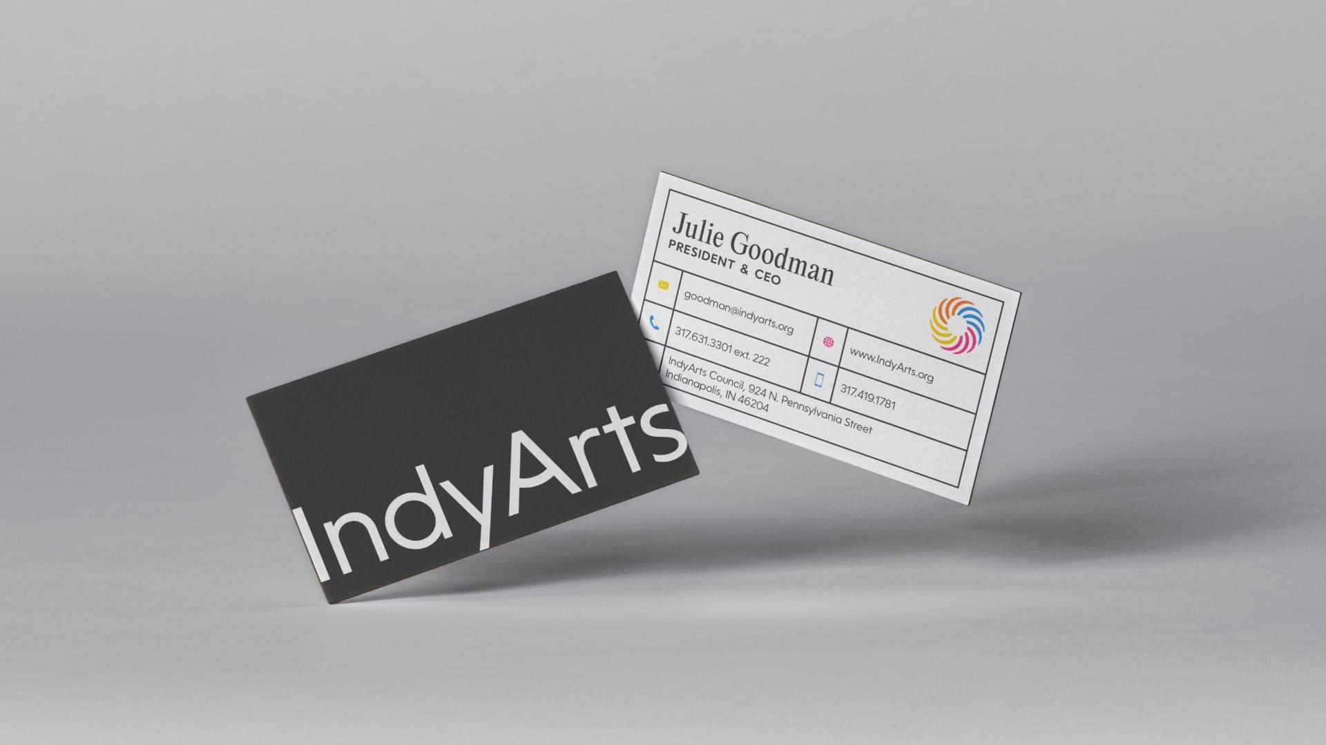 Two IndyArts business cards, one dark with the IndyArts wordmark and one white with contact details and the colorful spiral mark
