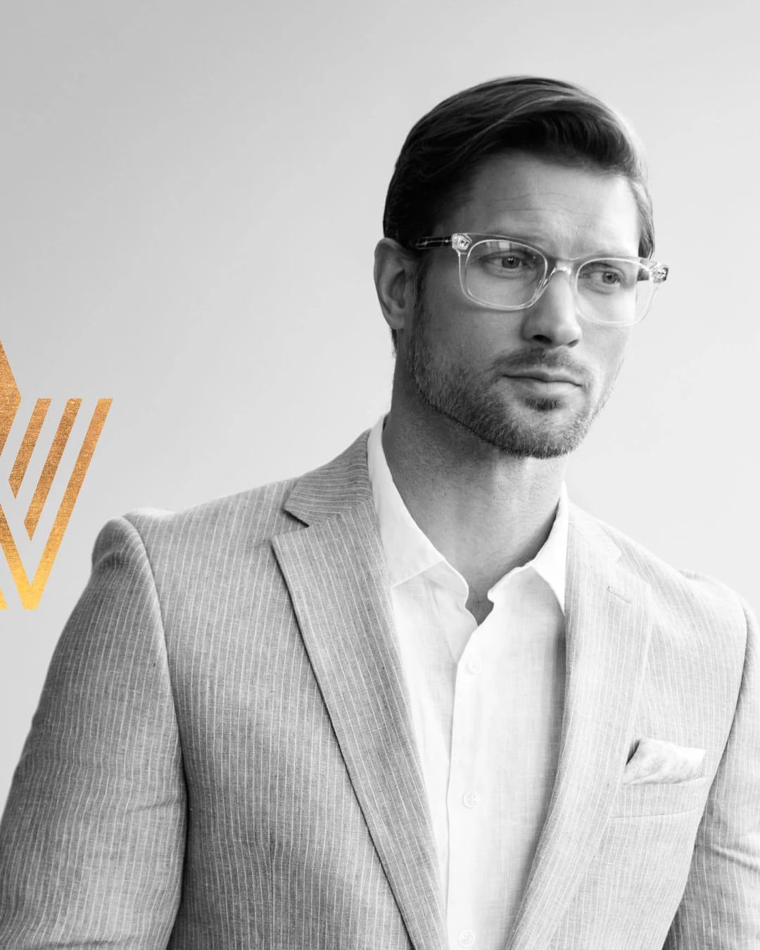 Black-and-white portrait of a man in clear Valdo glasses and a linen blazer, with the gold Valdo V mark