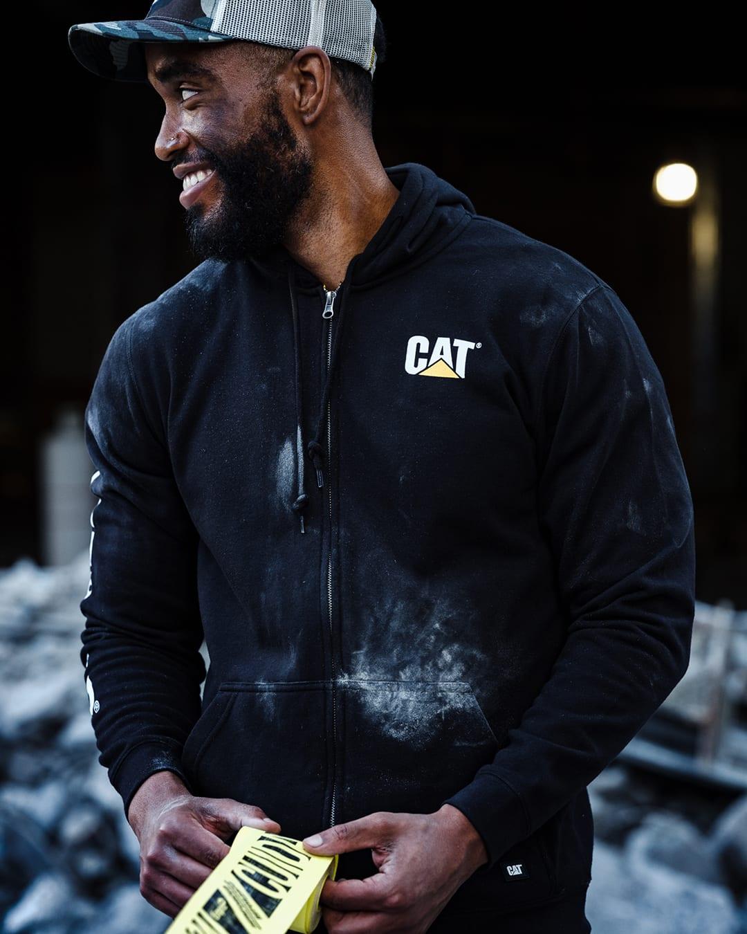 Smiling man in a black CAT zip hoodie and grey cap