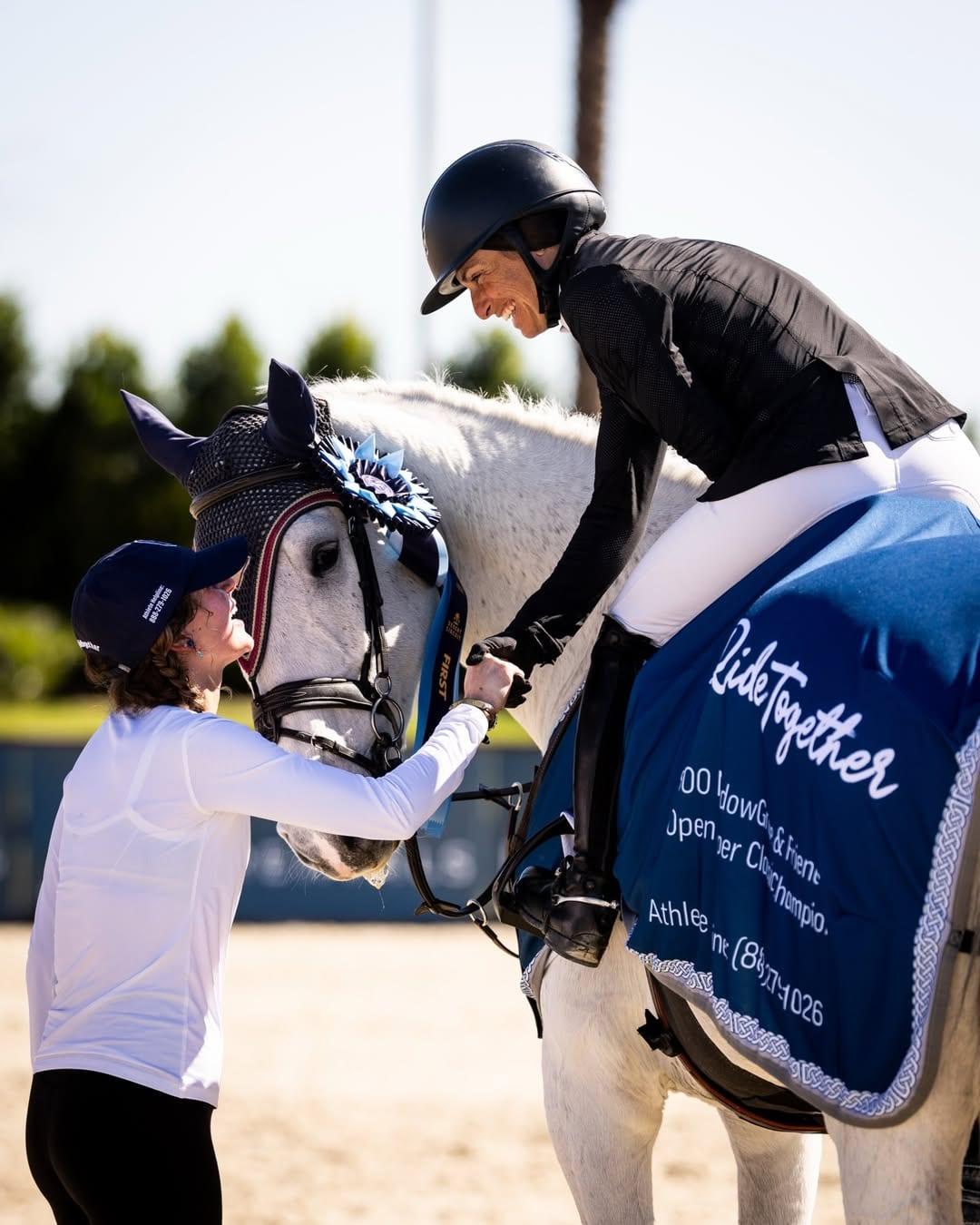 Equestrian rider on a grey horse wearing a #WeRideTogether saddle pad, greeting a woman beside the horse