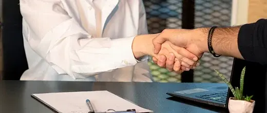 Two people shaking hands across a desk