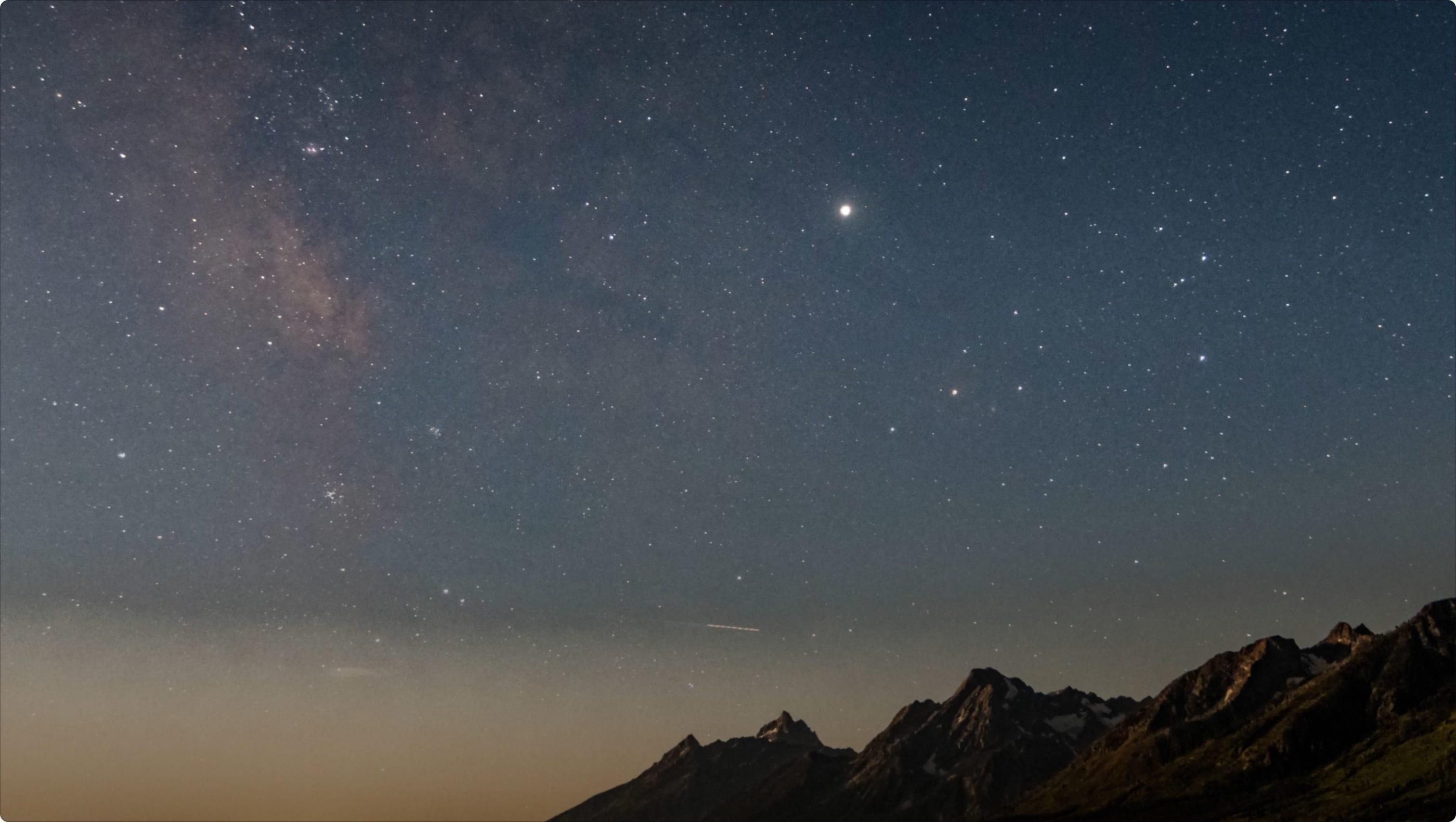 Starry night sky with the Milky Way and a bright star above a mountain ridge