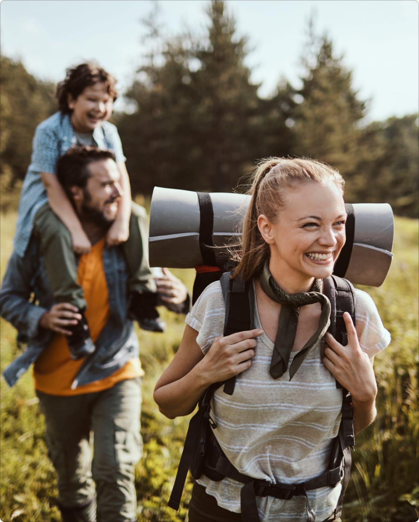 Smiling family hiking through a sunny meadow, a child riding on a father's shoulders