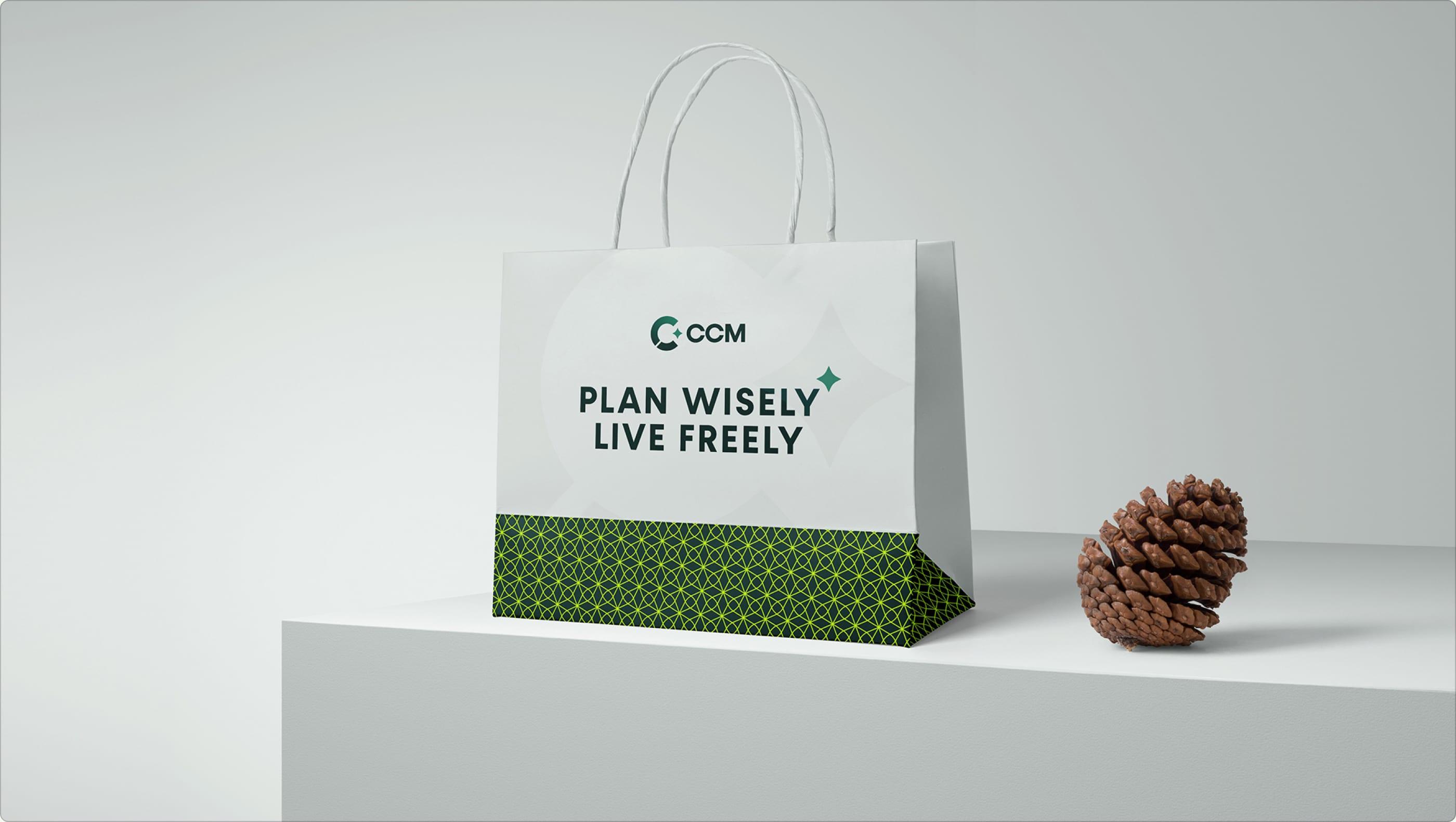 White CCM shopping bag with the "Plan Wisely, Live Freely" tagline beside a pine cone