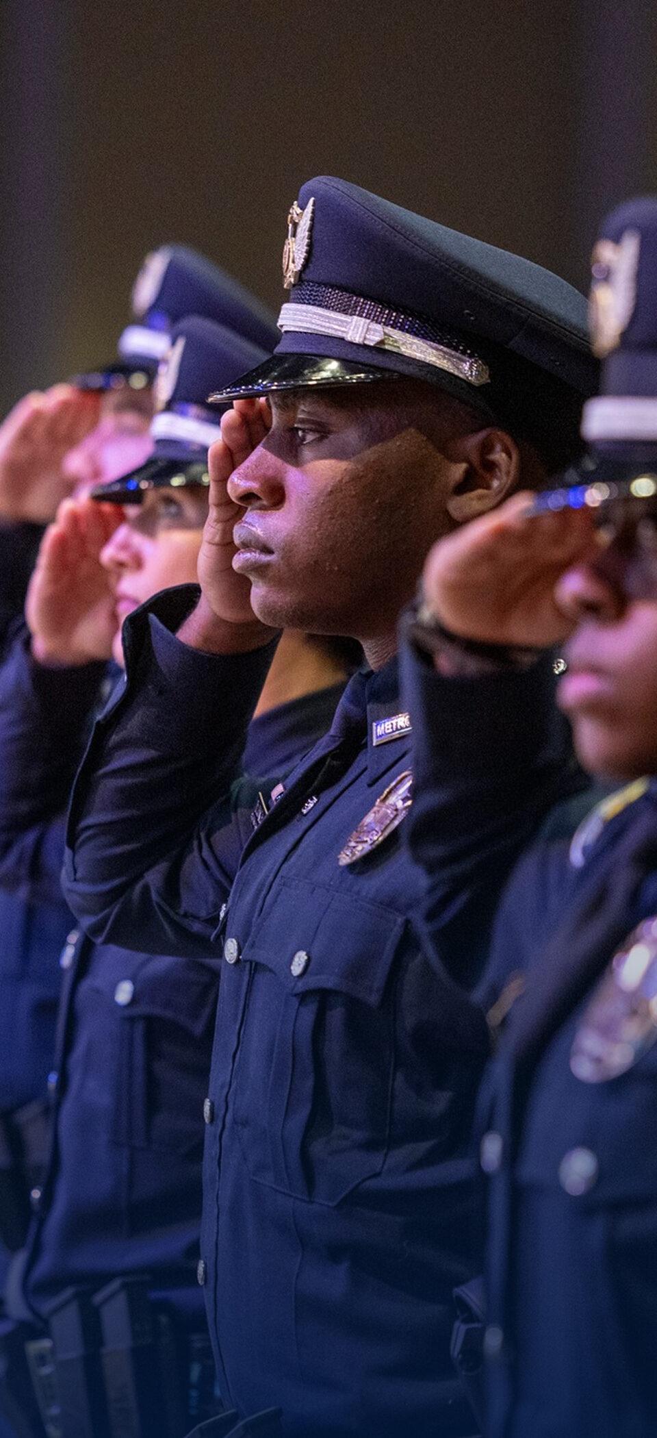 A row of LMPD recruits in dress uniforms and caps saluting at a graduation ceremony