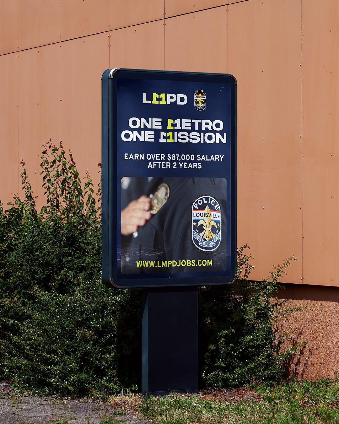 Street-side One Metro One Mission poster showing an officer's badge and lmpdjobs.com