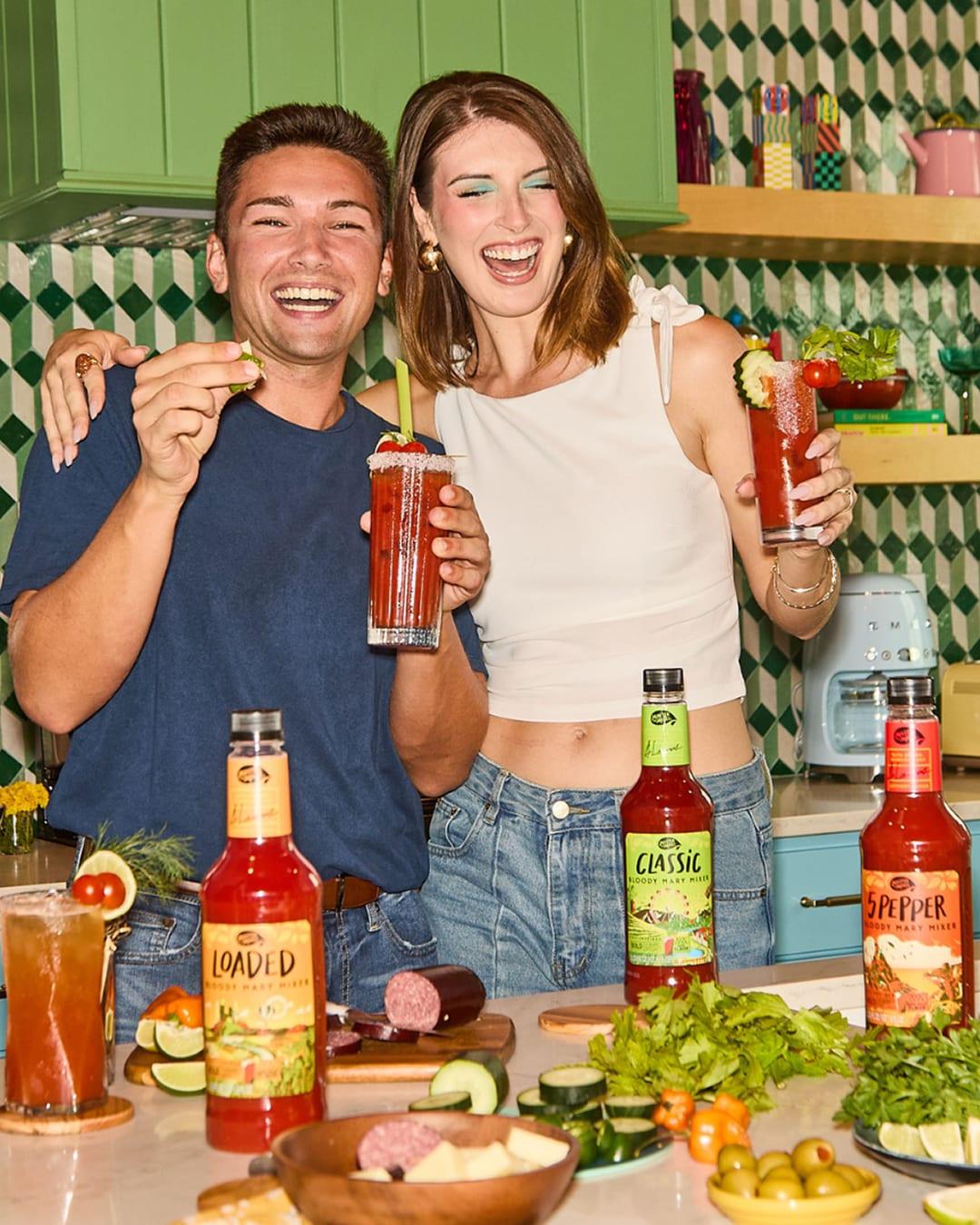Two friends laughing with cocktails beside Master of Mixes Bloody Mary mixer bottles