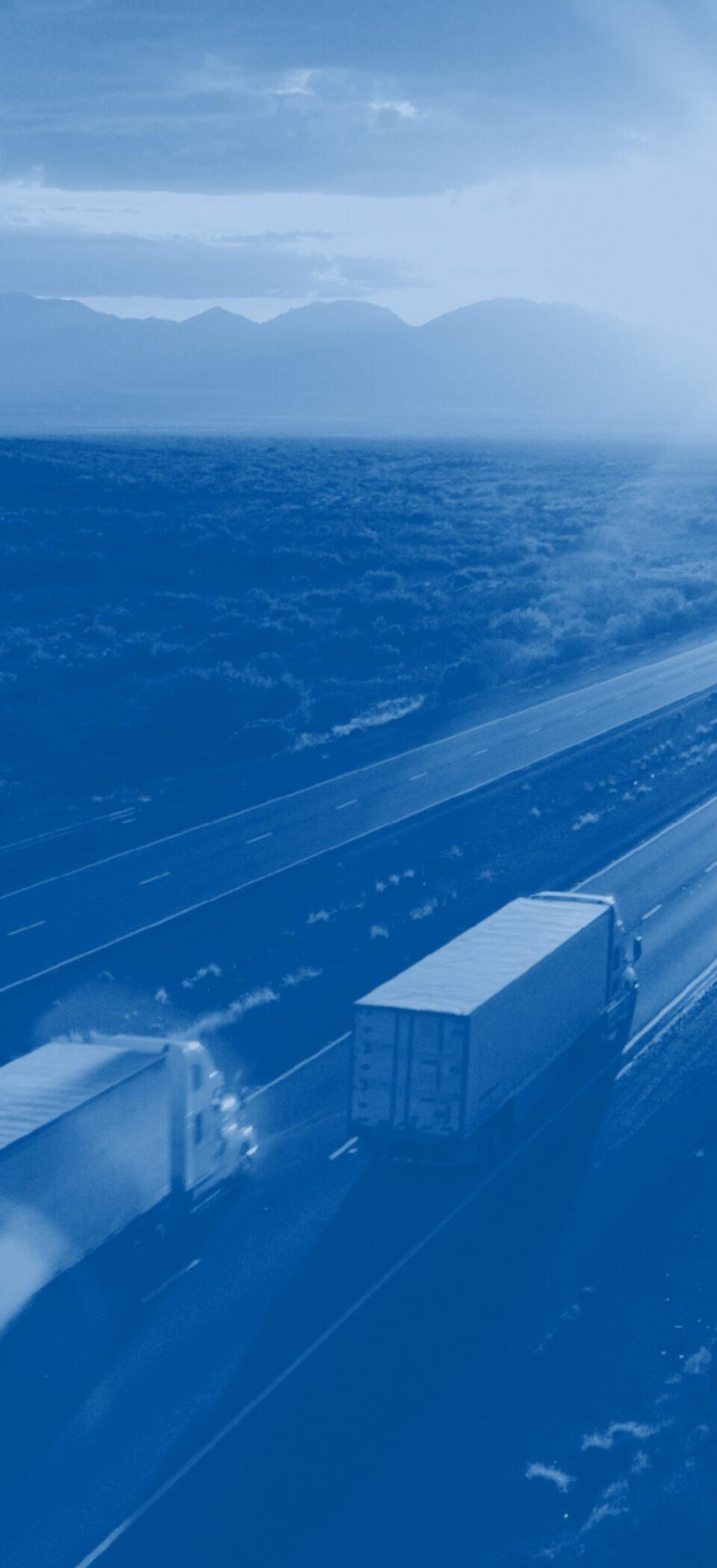 Semi trucks travelling a desert highway toward a mountain range at sunrise, tinted TForce blue